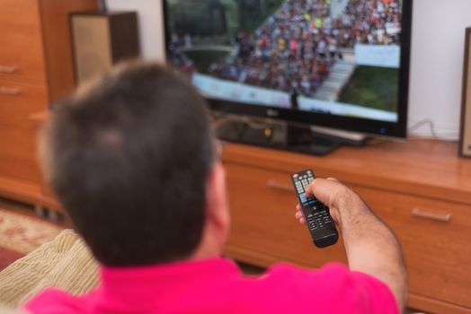 Back view of senior man watching tv holding remote control