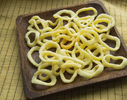 Delicious crispy rings of onion chips lie on a dark wooden plate on a yellow napkin background.