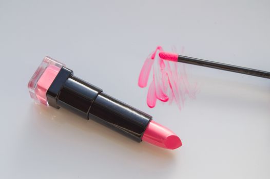 beautiful pink lip gloss smear with brush and a tube of lipstick, on a white background.