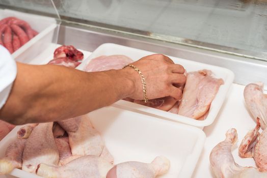 Butcher serving fresh chicken meat at display in butchery