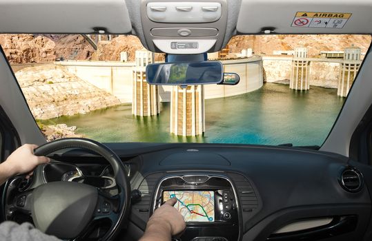 Driving a car while using the touch screen of a GPS navigation system towards Hoover Dam and Colorado River at the border between Nevada and Arizona, USA