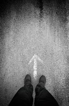 Feet in front of an arrow, detail of a direction arrow, sign