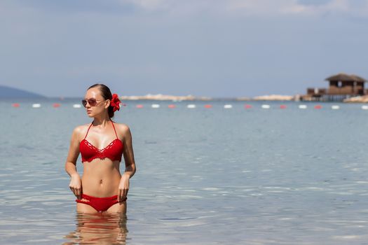 Beautiful woman walking in sea waterLovely young lady in red knitted swimwear looking away and walking in sea water while relaxing in wonderful resort