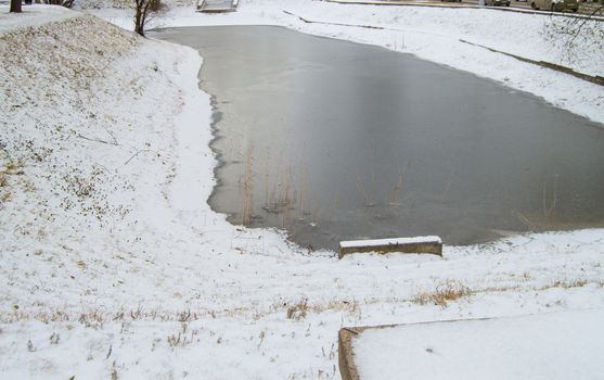 Frozen pond covered with the first snow in the city Park.