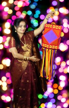 An Indian woman holding a traditional lantern during Diwali festival in India, on a background of colorful blur lights