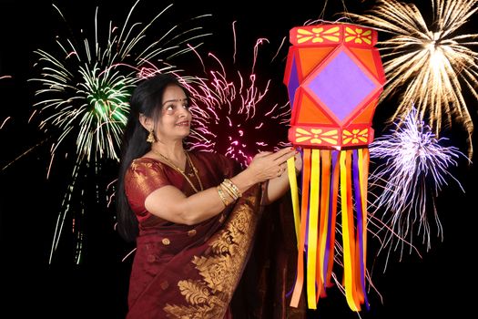 An Indian woman looking at the traditional Diwali lantern during Diwali festival in India, on the backdrop of Diwali fireworks.