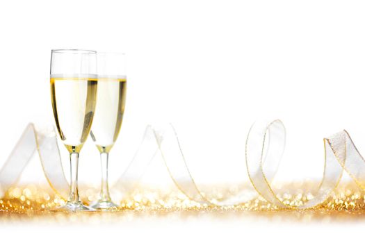 Glasses of champagne and ribbon on golden glitters isolated on white