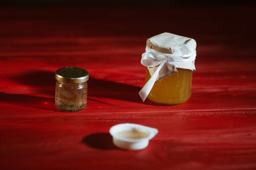 Hand with dipper picking honey from a jar of honey. Jars of honey, bee honeycomb and bee pollen on wooden table