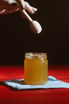 Hand with dipper picking honey from a jar of honey. Jars of honey, bee honeycomb and bee pollen on wooden table