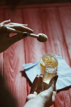 Hand with dipper picking honey from a jar of honey. Jars of honey, bee honeycomb and bee pollen on wooden table