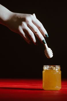 Hand with dipper picking honey from a jar of honey. Jars of honey, bee honeycomb and bee pollen on wooden table