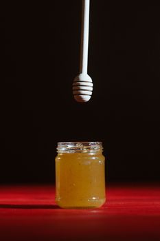 Hand with dipper picking honey from a jar of honey. Jars of honey, bee honeycomb and bee pollen on wooden table