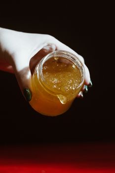 Hand with dipper picking honey from a jar of honey. Jars of honey, bee honeycomb and bee pollen on wooden table