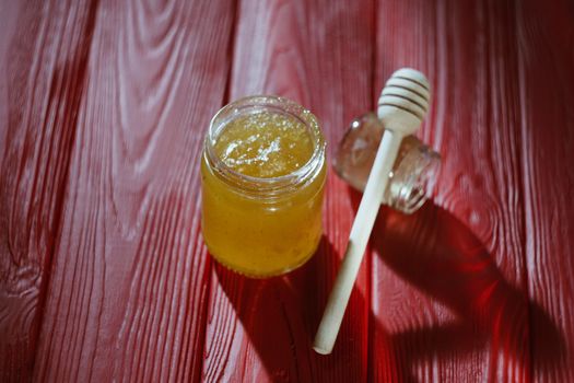 Hand with dipper picking honey from a jar of honey. Jars of honey, bee honeycomb and bee pollen on wooden table