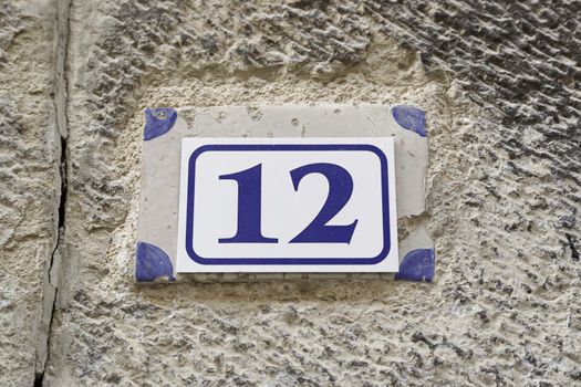Number twelve on a plate on a wall, detail of a number of information in a house in the city