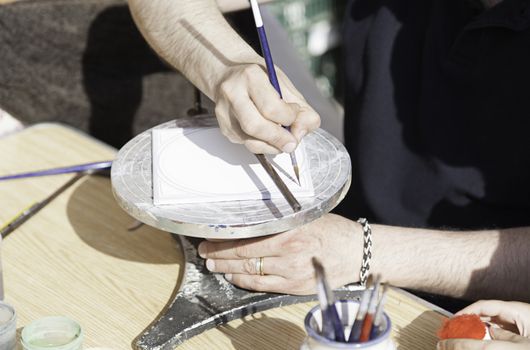 Hand painting a plate, detail of a craftsman decorating a ceramic dish, traditional art
