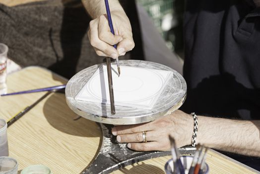 Hand painting a plate, detail of a craftsman decorating a ceramic dish, traditional art