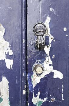 Old knocker shaped like a hand, detail of an old blue door with a metal knocker