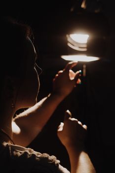 girl reaching for the light of the lantern, wooman in a dark room. illuminated hands with spotlight