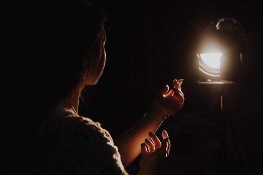 girl reaching for the light of the lantern, wooman in a dark room. illuminated hands with spotlight