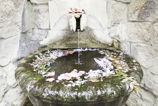 Old stone fountain with flowers, detail of a decorated stone sculpture, ancient atrte