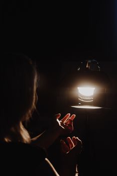 girl reaching for the light of the lantern, wooman in a dark room. illuminated hands with spotlight