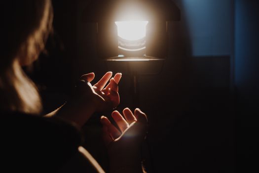 girl reaching for the light of the lantern, wooman in a dark room. illuminated hands with spotlight