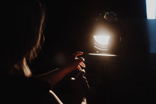 girl reaching for the light of the lantern, wooman in a dark room. illuminated hands with spotlight