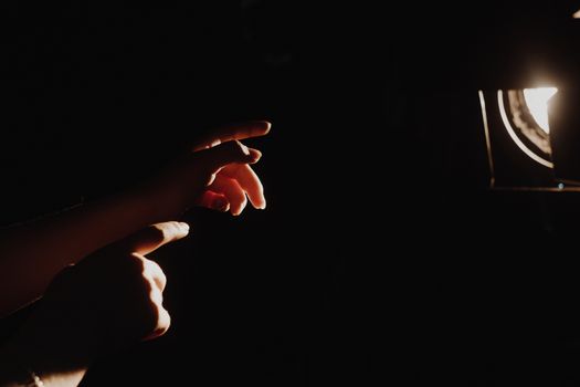 girl reaching for the light of the lantern, wooman in a dark room. illuminated hands with spotlight