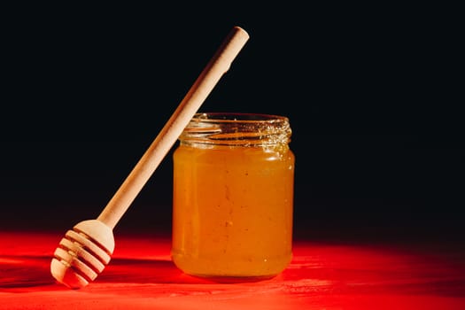 Honey with dipper on red wooden background with the the play of light and shadow