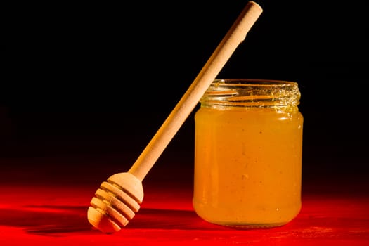 Honey with dipper on red wooden background with the the play of light and shadow