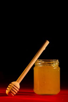 Honey with dipper on red wooden background with the the play of light and shadow