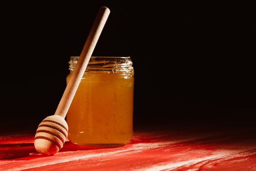 Honey with dipper on red wooden background with the the play of light and shadow