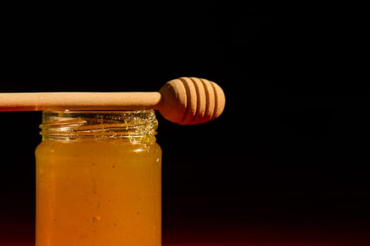 Honey with dipper on red wooden background with the the play of light and shadow