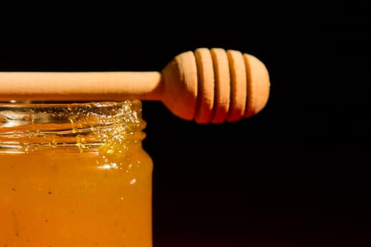 Honey with dipper on red wooden background with the the play of light and shadow