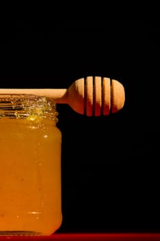 Honey with dipper on red wooden background with the the play of light and shadow