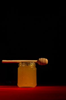 Honey with dipper on red wooden background with the the play of light and shadow