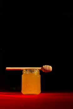 Honey with dipper on red wooden background with the the play of light and shadow