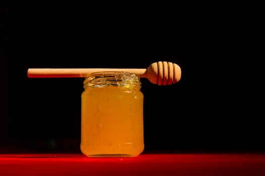 Honey with dipper on red wooden background with the the play of light and shadow