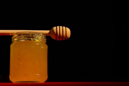 Honey with dipper on red wooden background with the the play of light and shadow