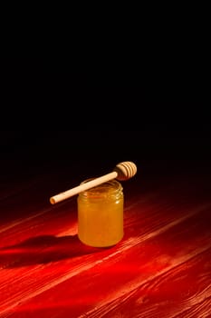 Honey with dipper on red wooden background with the the play of light and shadow