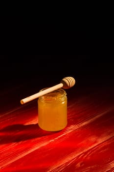 Honey with dipper on red wooden background with the the play of light and shadow