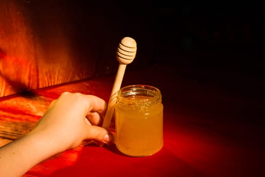 Honey with dipper on red wooden background with the the play of light and shadow