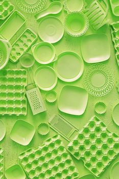 Close up flat lay of different green color painted kitchen utensils and tools, grater, spoon, egg carton, plastic disposable plates, elevated top view, directly above