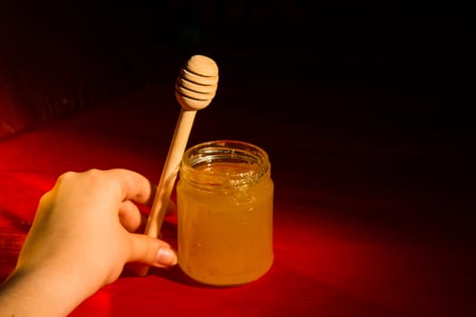 Honey with dipper on red wooden background with the the play of light and shadow