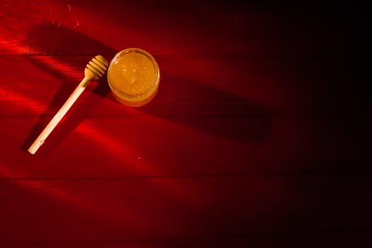 Honey with dipper on red wooden background with the the play of light and shadow