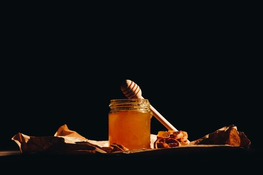 Honey with wooden honey dipper and fruits on wooden table close up