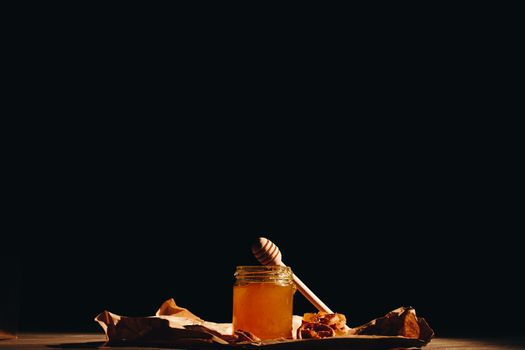 Honey with wooden honey dipper and fruits on wooden table close up