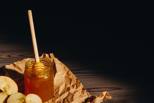 Honey with wooden honey dipper and fruits on wooden table close up