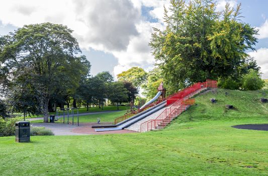 A large slide on a small hill and several swings at the entrance to Duthie park near Dee river, Aberdeen, Scotland